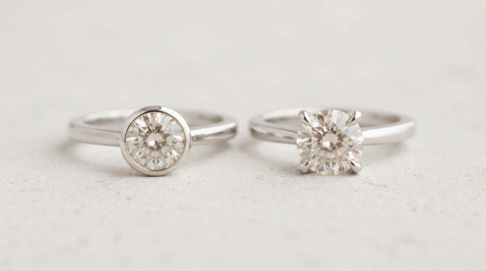 Two rings side by side, one with a flush bezel-set stone and one with a raised claw-set stone