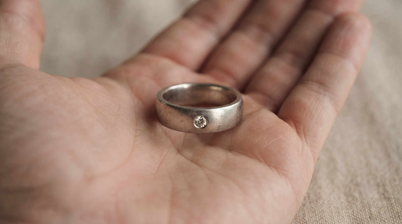 Memorial diamond set flush into a worn men's wedding band held in an open palm