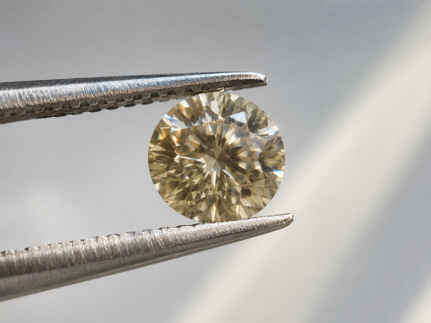 Close-up of a champagne-toned lab-grown memorial diamond held in tweezers under daylight